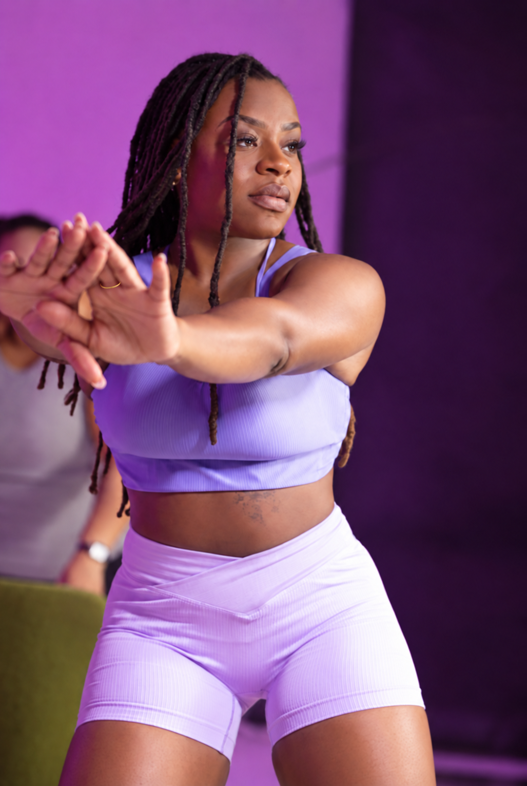 Coco stretching her arms in a lilac athletic outfit
